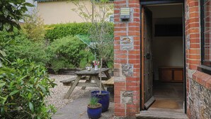A brick building with a wooden door, a small garden with a wooden bench, and a potted plant.