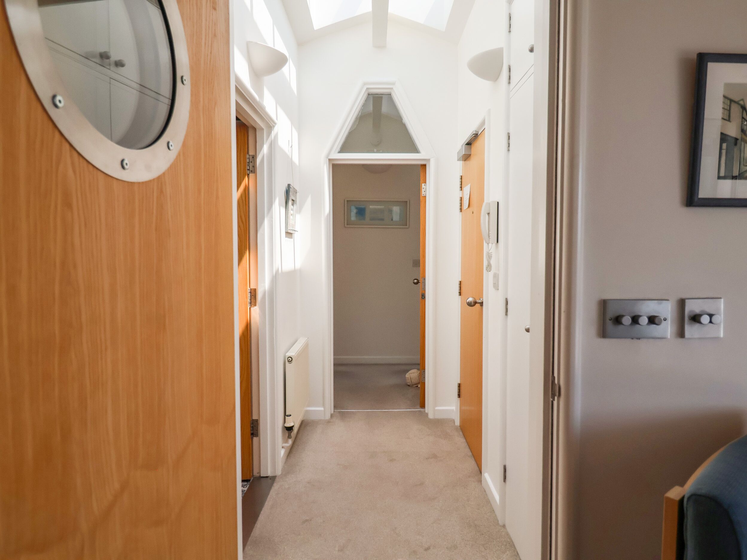 Un couloir étroit avec des portes en bois, un radiateur et un tableau encadré accroché au mur.