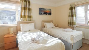 A hotel room with two beds, a painting of a sunset, and a window with curtains. - Greystones (Lyme Regis)