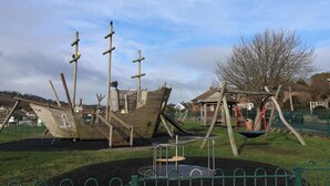 A playground with a pirate ship play structure, swings, and a small slide. - Greystones (Lyme Regis)