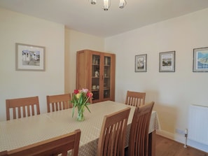 A dining area with a table set for six, surrounded by wooden chairs. A cabinet with glass doors is visible in the background. - Greystones (Lyme Regis)