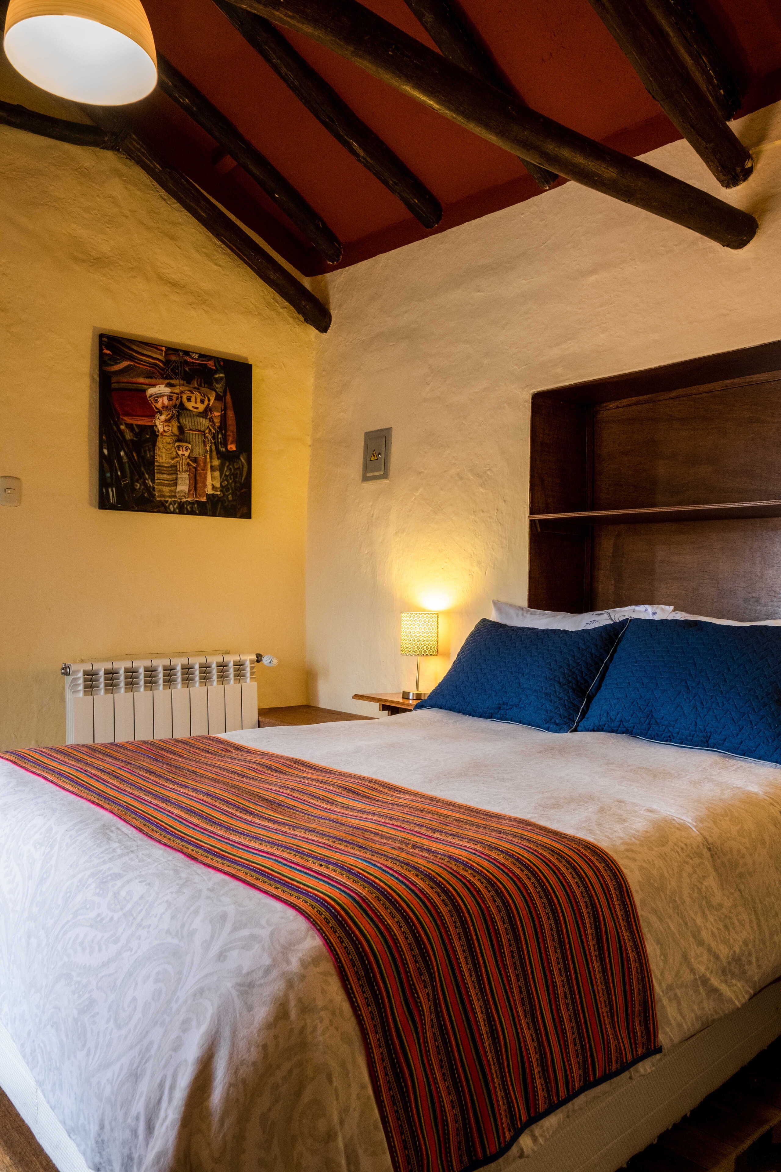A bedroom with a bed, a headboard, a wall-mounted painting, a bedside lamp, and a radiator.