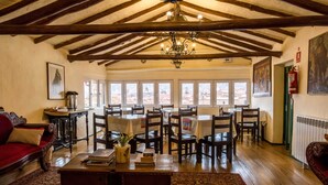 A spacious room with wooden beams, a chandelier, and a view through large windows. - Hostal Corihuasi (Cusco)