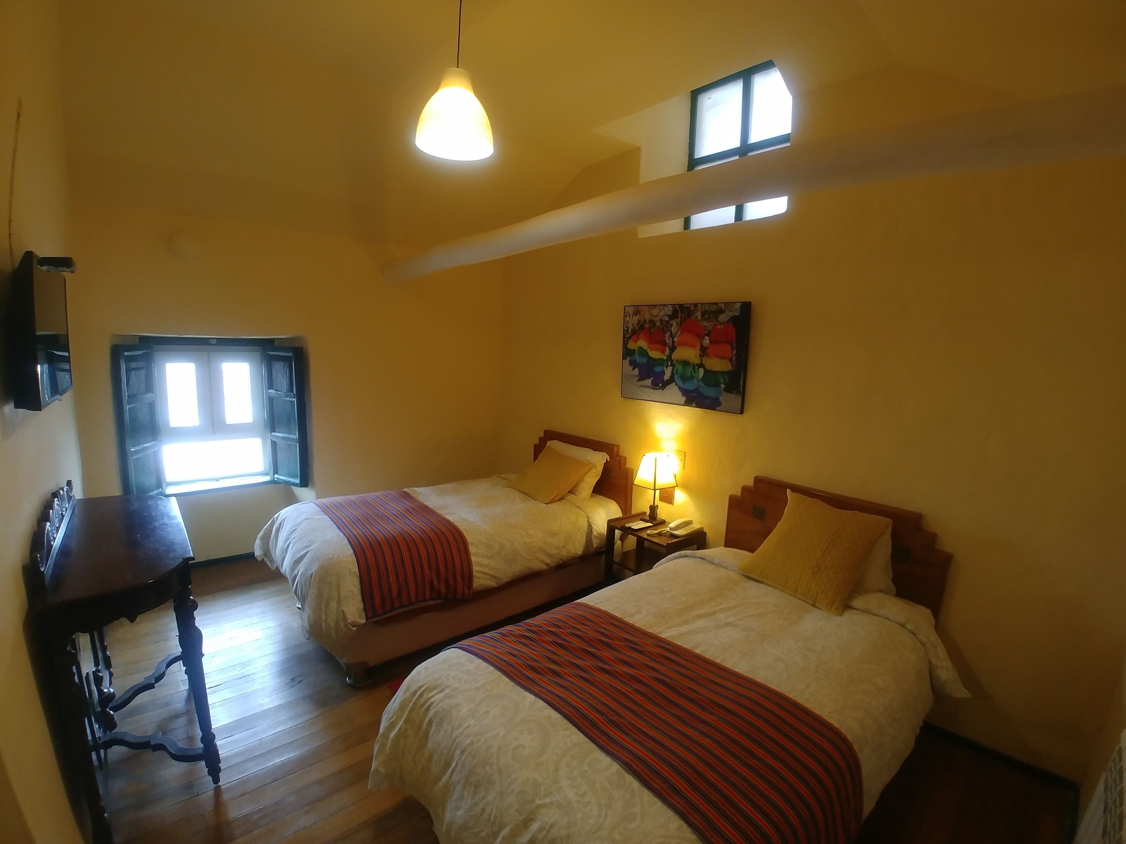 A hotel room with two beds, a desk, a lamp, and a painting on the wall.