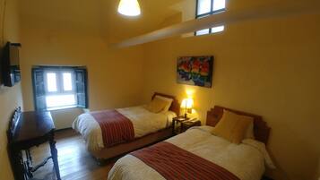 A hotel room with two beds, a desk, a lamp, and a painting on the wall.