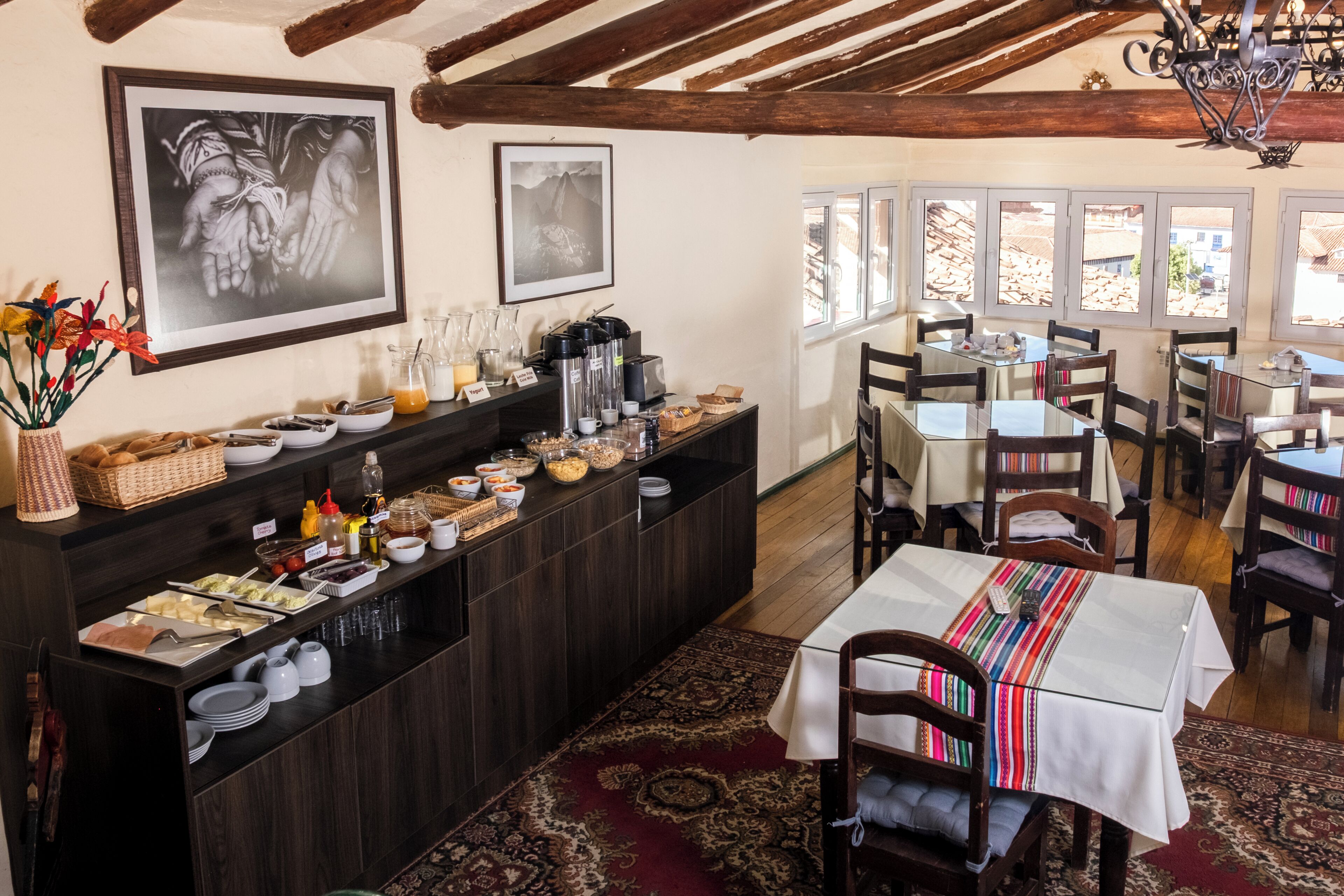 A dining area with a buffet, wooden tables, chairs, and a view of mountains through the windows.