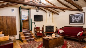 A cozy living room with a wooden ceiling, a red sofa, a wooden coffee table, a TV, and a staircase leading to an upper floor. - Hostal Corihuasi (Cusco)