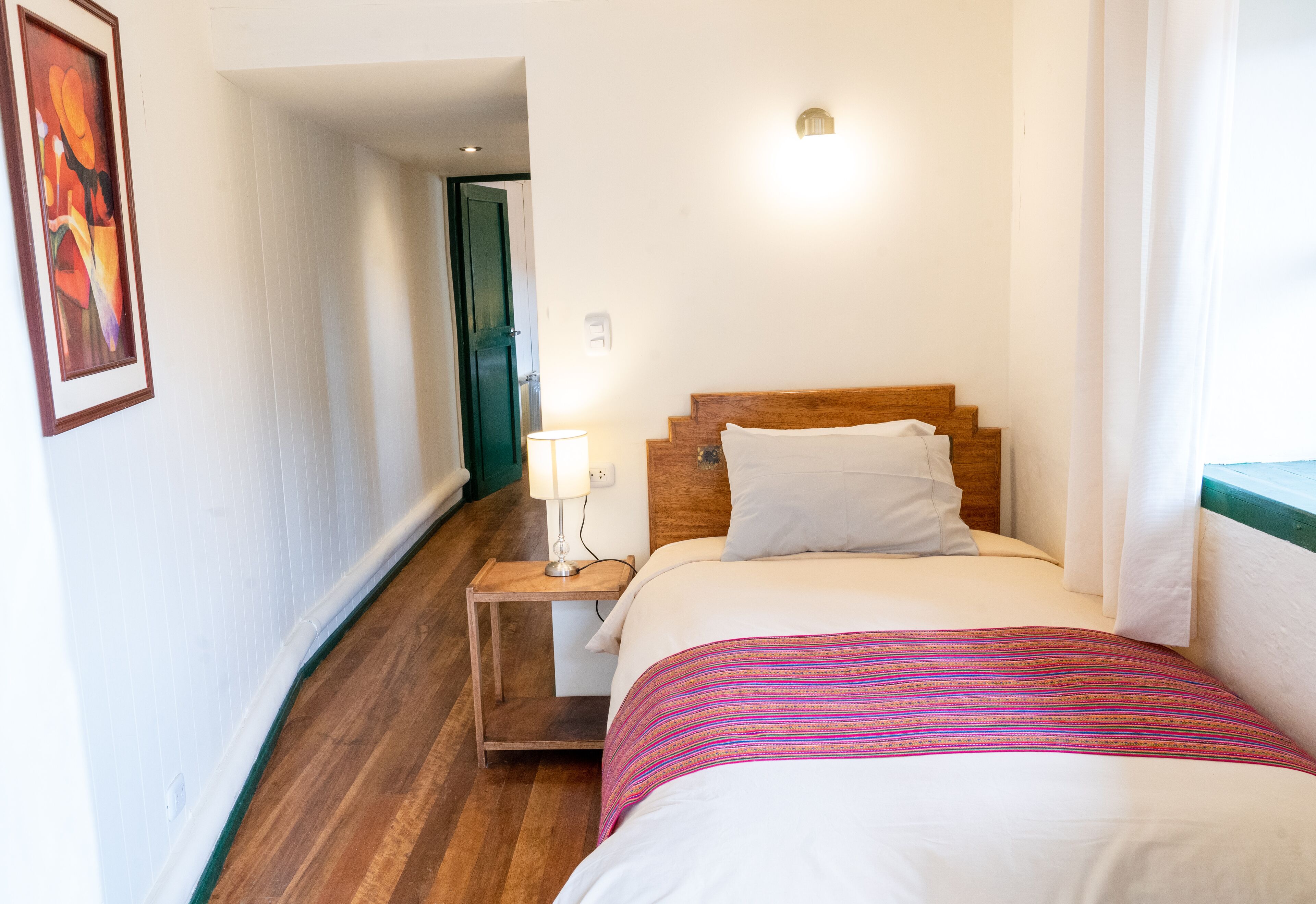 A hotel room with a wooden bed, a nightstand with a lamp, and a framed picture on the wall.