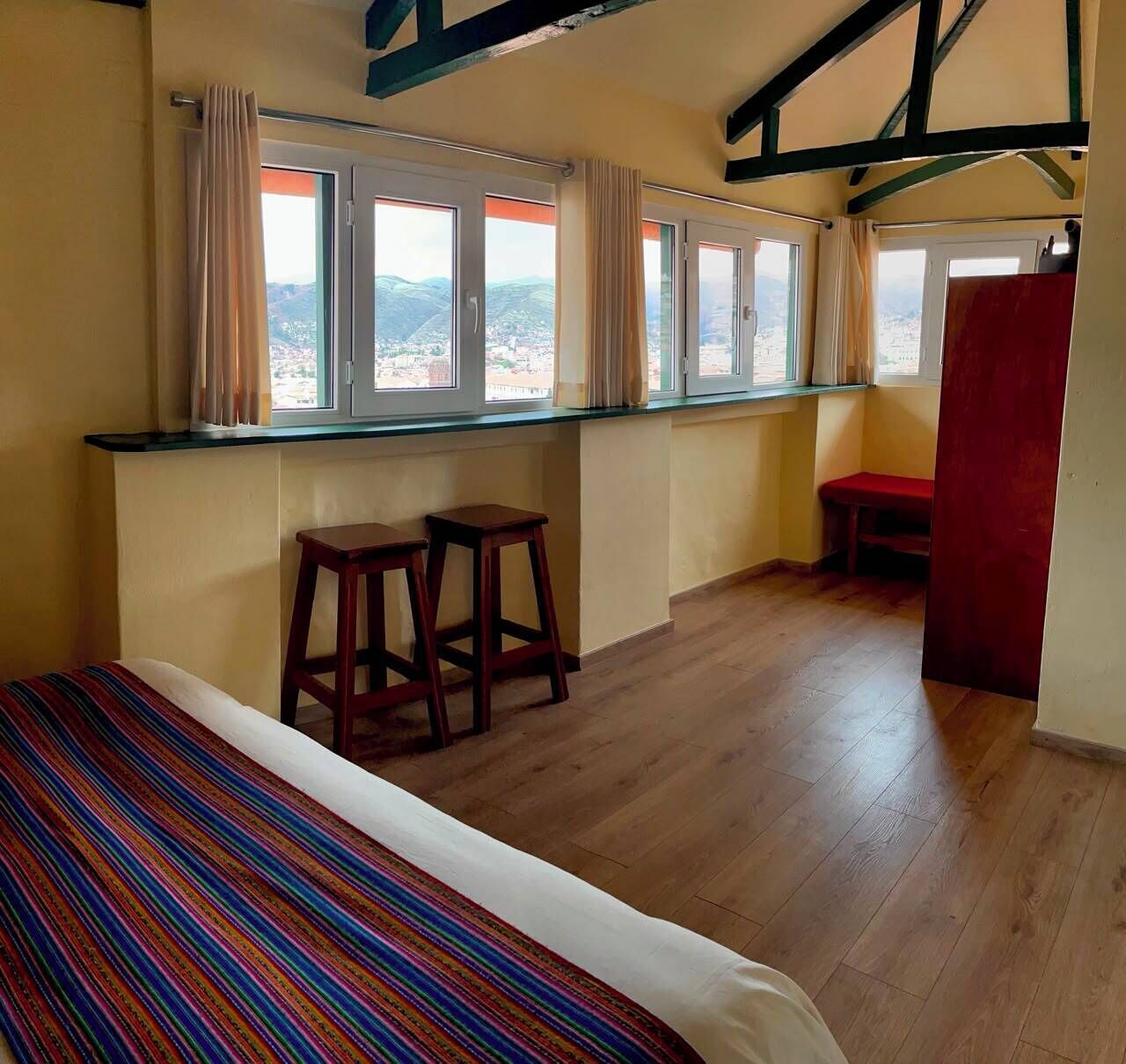 Una habitación con una cama, dos taburetes, un banco y un ventanal con vistas.