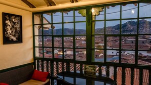 A room with a view of a cityscape through a window with a grid pattern. - Hostal Corihuasi (Cusco)