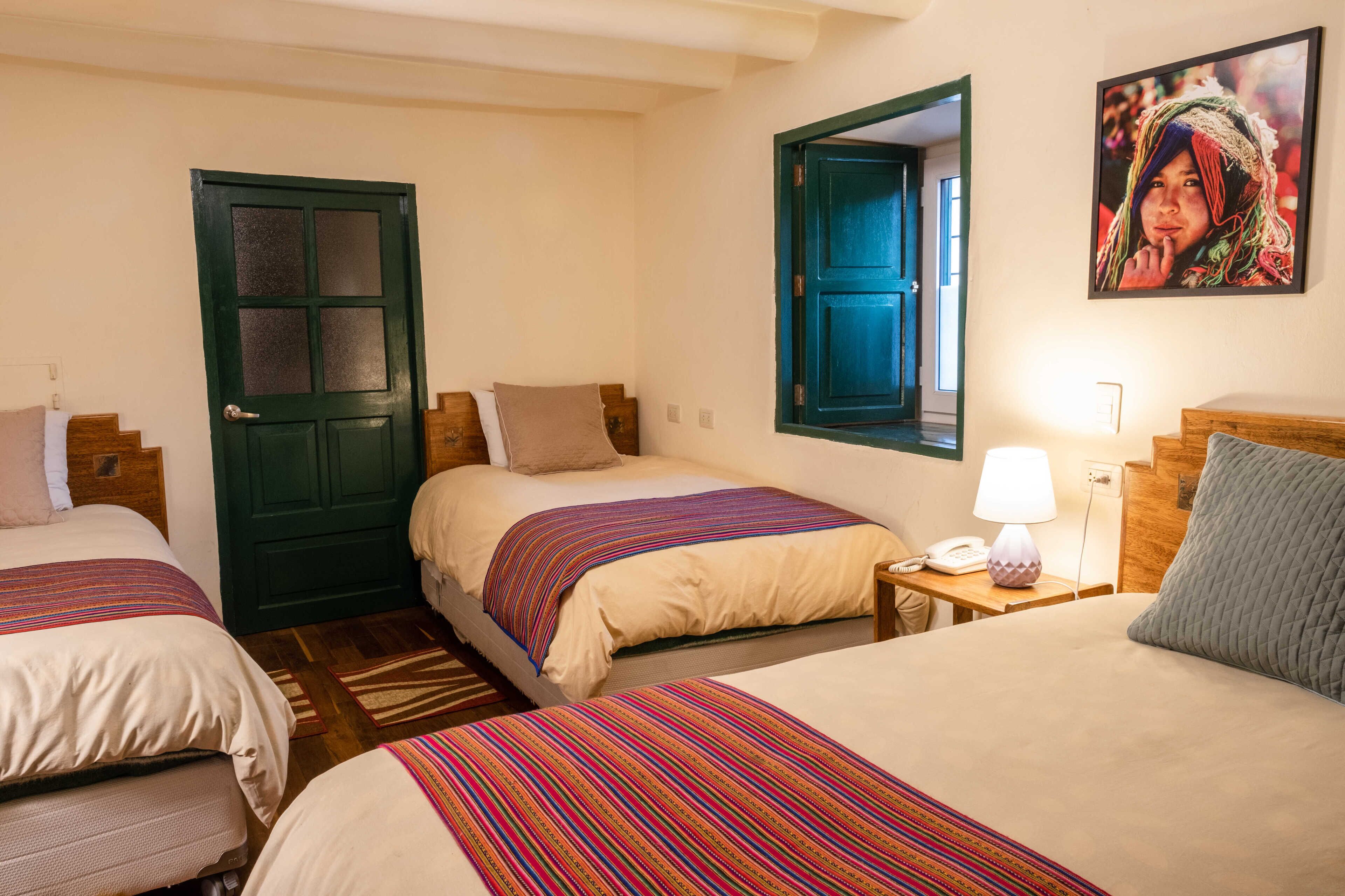 A hotel room with three beds, a wooden headboard, a nightstand with a lamp, and a framed picture on the wall.