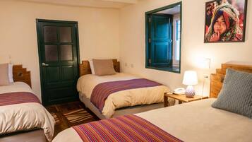 A hotel room with three beds, a wooden headboard, a nightstand with a lamp, and a framed picture on the wall.