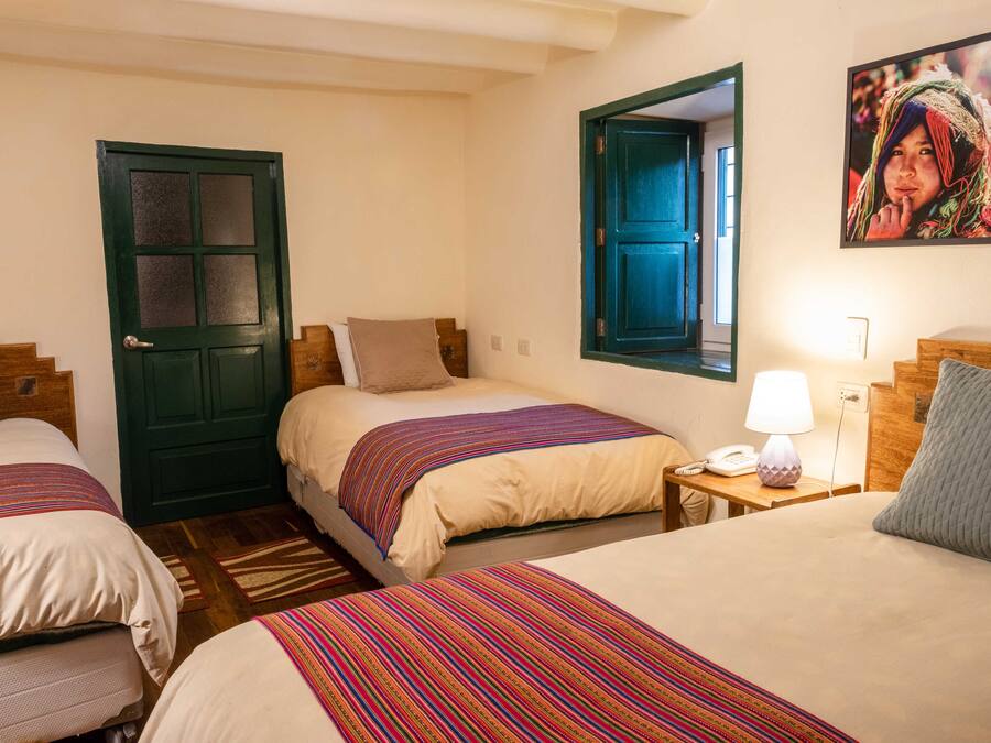 A hotel room with three beds, a wooden headboard, a nightstand with a lamp, and a framed picture on the wall.