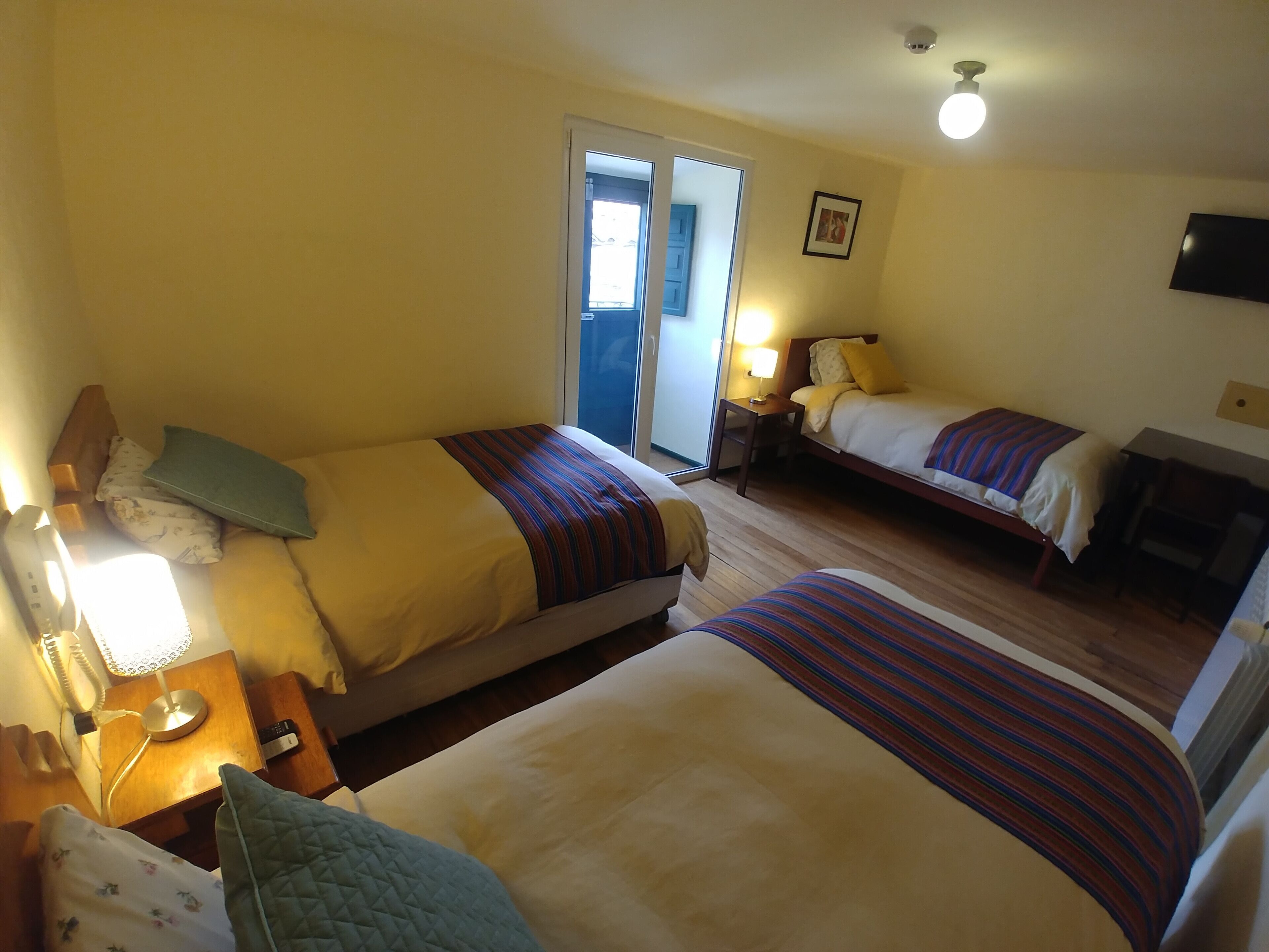 A hotel room with two beds, a desk, a chair, a TV, and a sliding door to the outside.