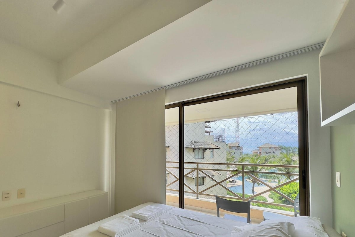 A hotel room with a large sliding glass door leading to a balcony with a view of buildings and a pool.