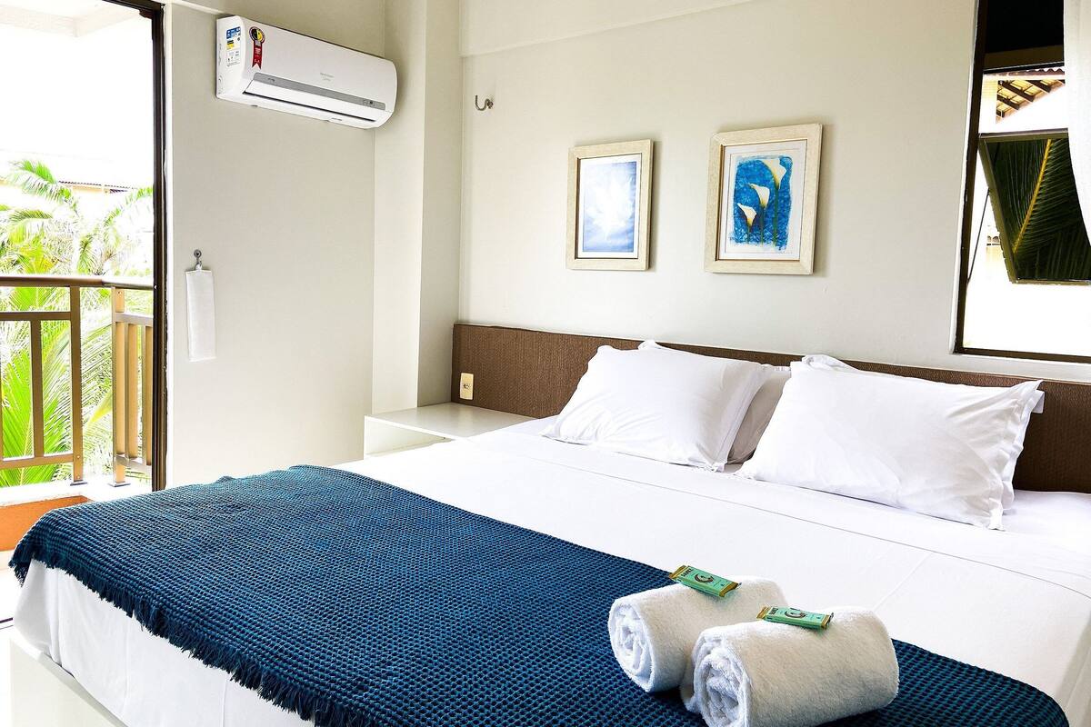 A hotel room with a bed, air conditioning unit, artwork, and a balcony.