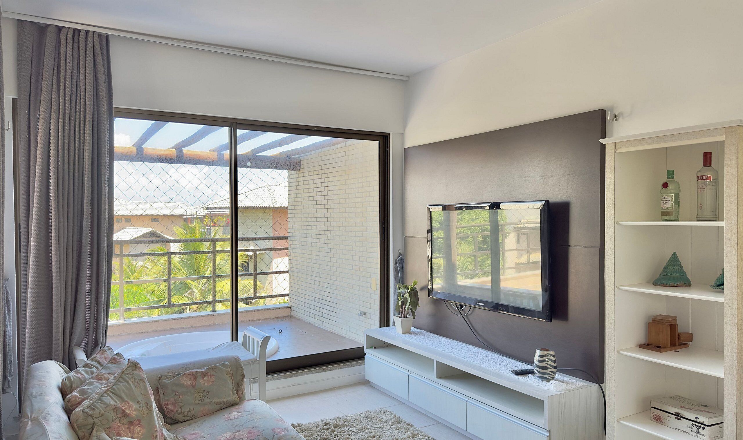 A modern living room with a large TV, a sofa, a balcony with a view, and a shelf with items.