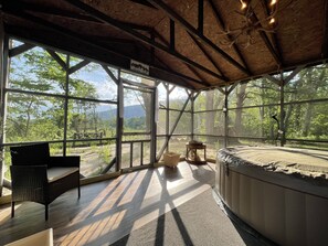 Una cabaña rústica con un gran ventanal, una silla de mimbre, una mesa redonda y un jacuzzi.