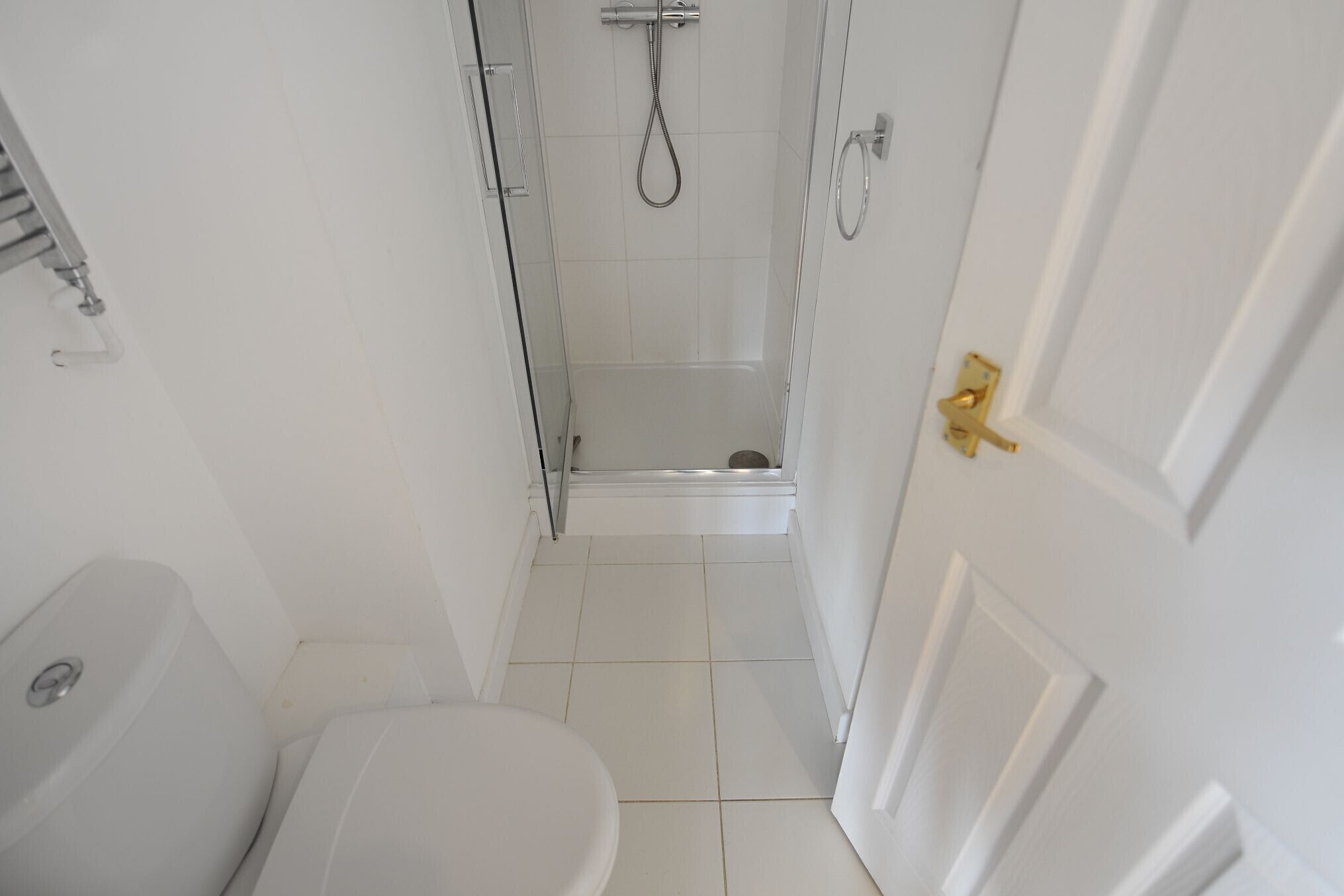 Un baño estrecho con inodoro, ducha y puerta con pomo dorado.