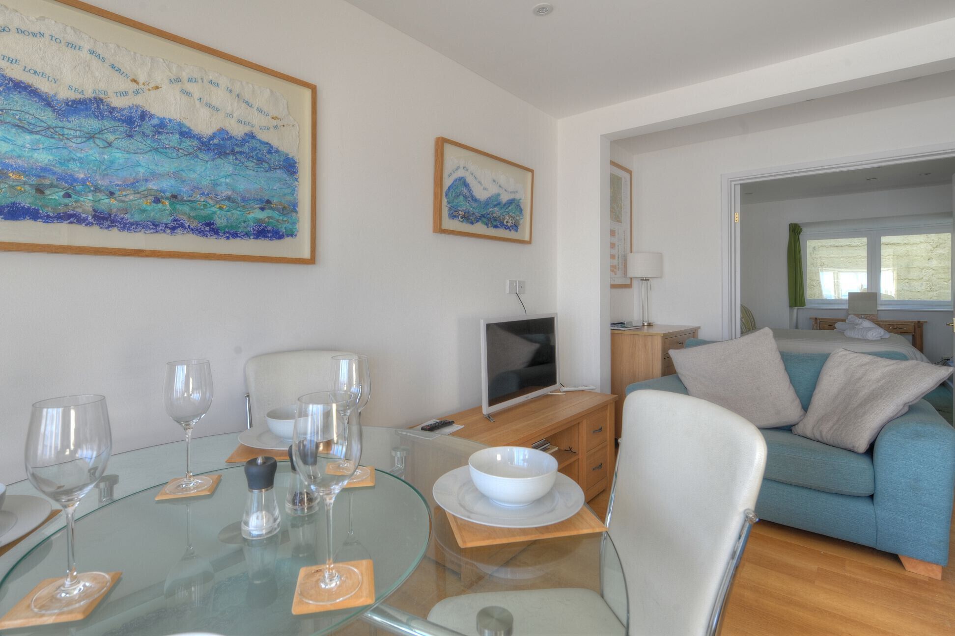 Een moderne woonkamer met een glazen eettafel, zitplaatsen, een flatscreen televisie en een bank.
