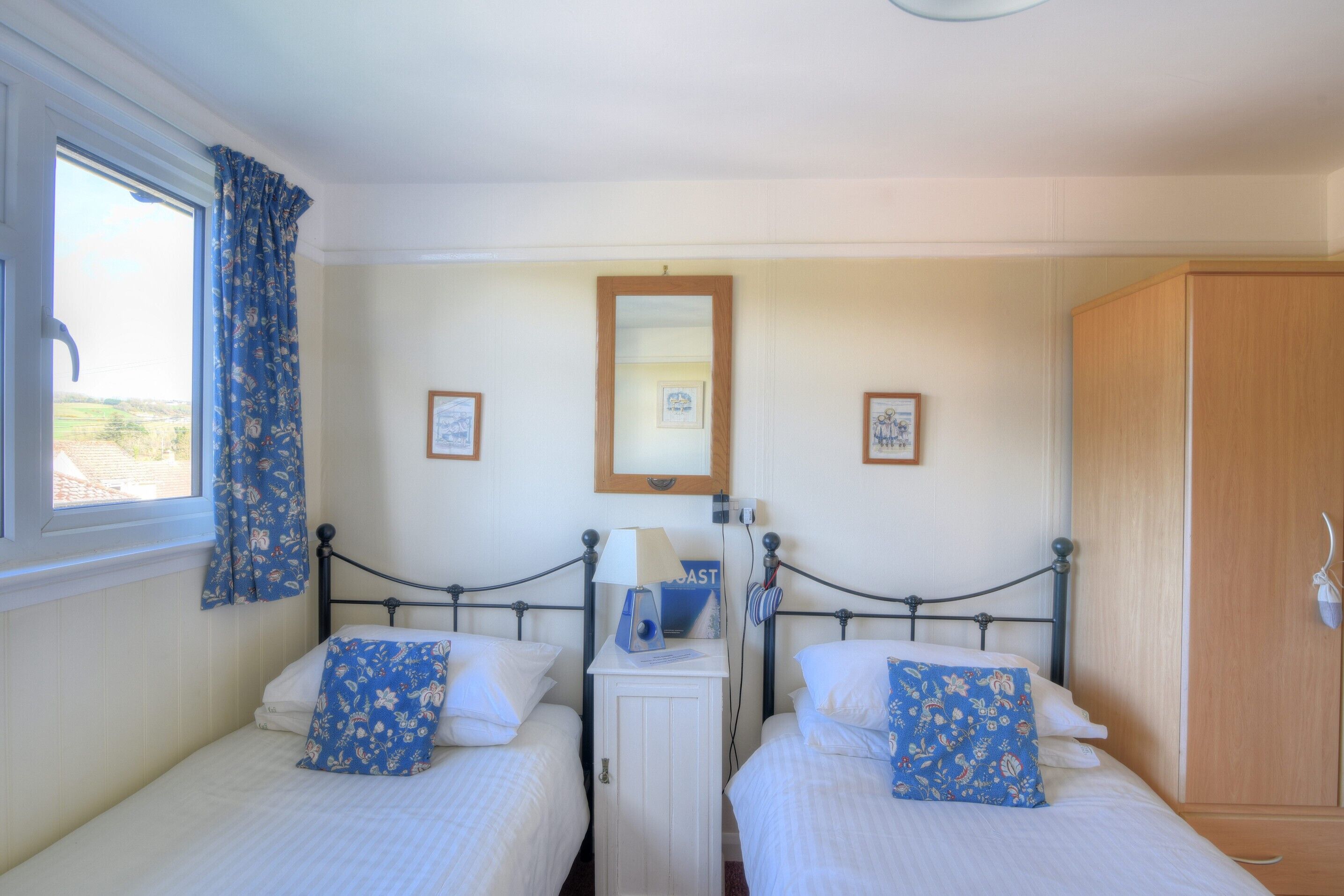 A bedroom with two single beds, a wooden wardrobe, and a small cabinet with a mirror and framed pictures.