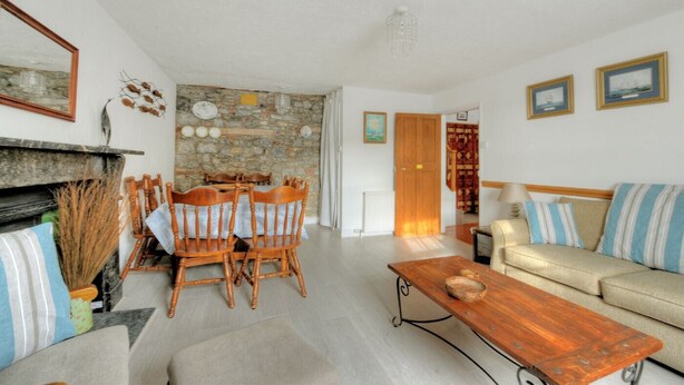 A living room with a stone wall, wooden dining table, and a sofa with striped cushions. - Waltham House (Lyme Regis)