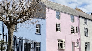 A two-story building with a pink and blue facade, a black metal fence, and a tree with bare branches. - Waltham House (Lyme Regis)