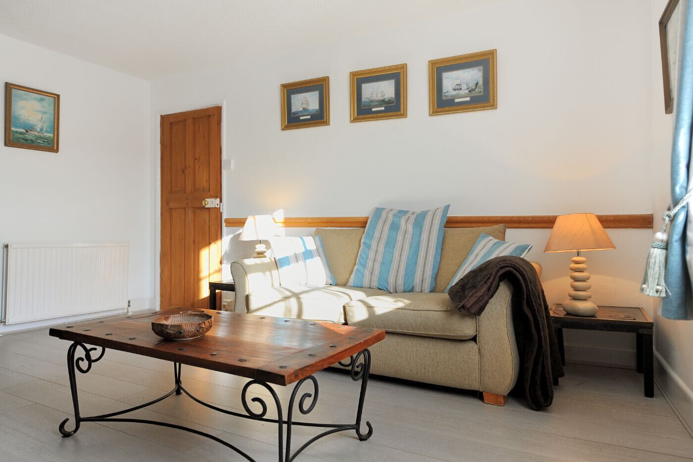 A living room with a wooden table, a sofa with striped cushions, and three framed pictures on the wall.
