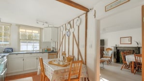 A traditional kitchen with wooden beams, a dining area with a table set for two, and a fireplace in the living room. - Waltham House (Lyme Regis)