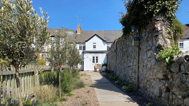 A narrow stone pathway leading to a white building with a pitched roof. - 12 Mill Green (Lyme Regis)