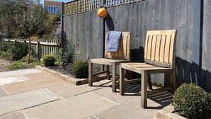 An outdoor seating area with two wooden chairs and a small table, a wooden fence, and a potted plant. - 12 Mill Green (Lyme Regis)