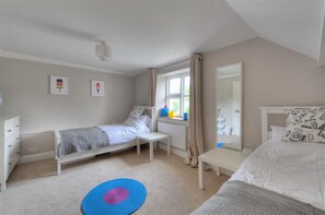 A bedroom with a single bed, a bedside table, a window with curtains, a radiator, and a mirror. - Mermaid House (Lyme Regis)
