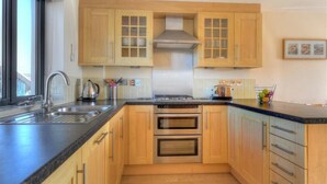 Una cocina con armarios de madera, una campana de acero inoxidable, un horno doble, un lavamanos y una ventana.