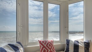 Une pièce avec vue sur la mer, grâce à une grande baie vitrée, agrémentée d’un tapis blanc moelleux et de deux coussins.