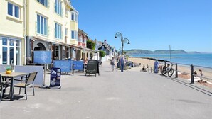 Une promenade en bord de mer, bordée d’immeubles, avec une plage et un ciel dégagé.