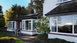 A two-story house with a conservatory, a patio with chairs, and a garden. - West Ridge Bungalow (Seaton)