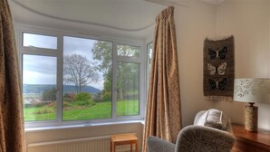 A room with a large window, a chair, a small table, and a lamp. - West Ridge Bungalow (Seaton)