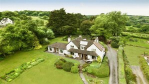 A large, white, two-story house with a well-maintained lawn and garden, surrounded by trees and open fields. - West Ridge Bungalow (Seaton)