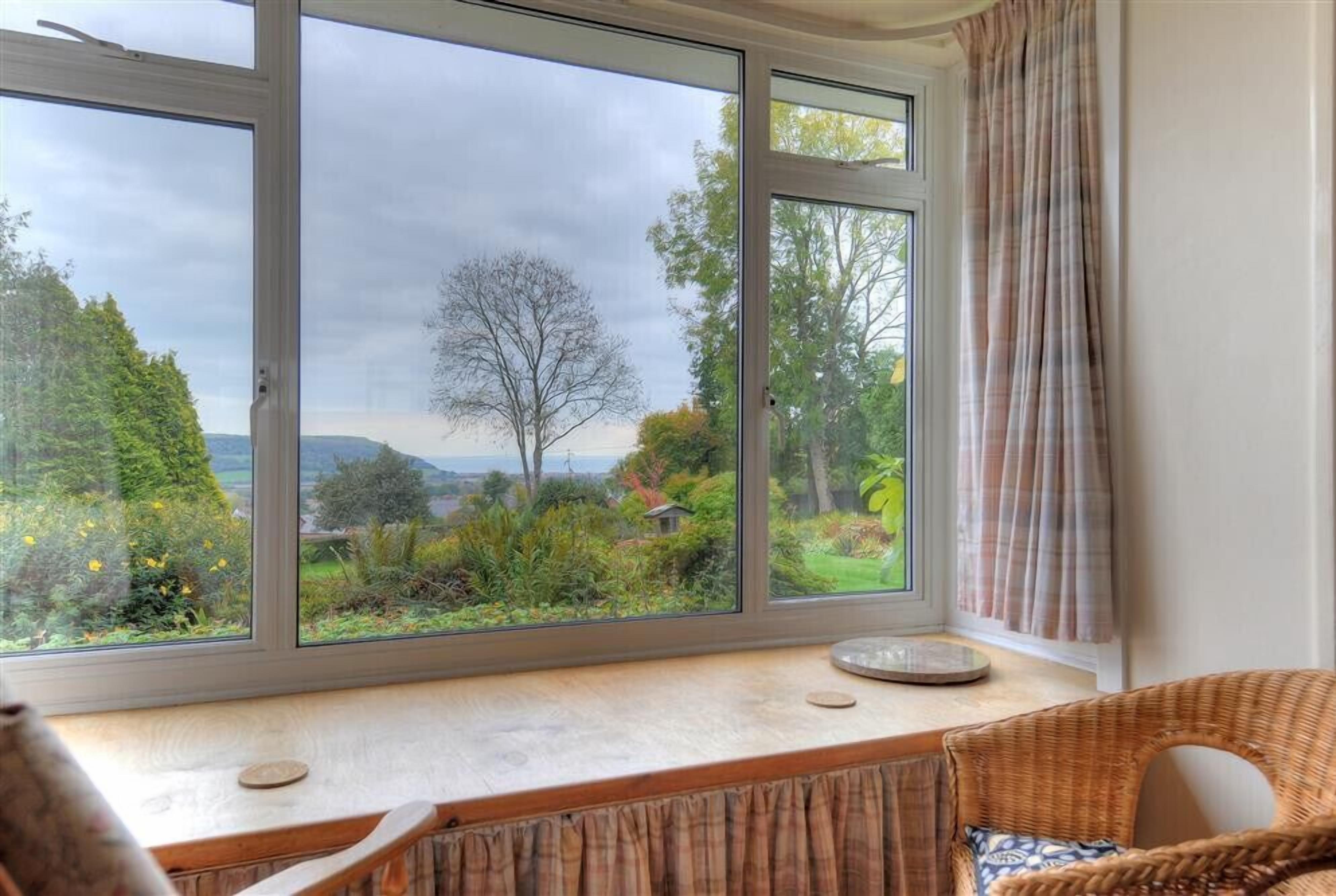 A room with a large window offering a view of a garden and hills.