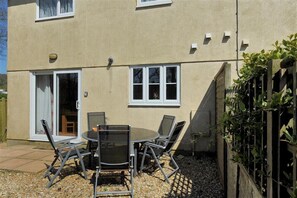A patio with a round table and chairs, a sliding glass door, and a small garden area with a wooden fence. - 4 Riverside Cottages (Bridport)