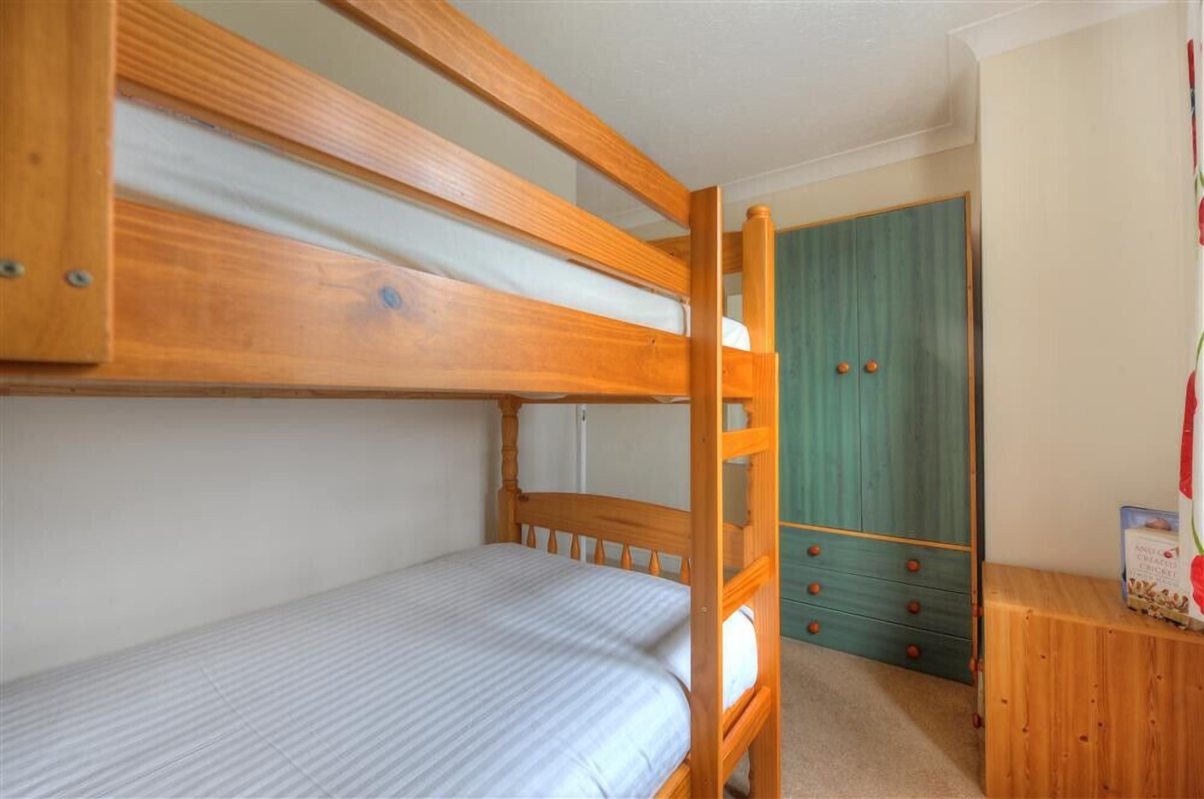 Un lit superposé avec une structure en bois, un lit simple en dessous et une armoire verte avec des tiroirs.