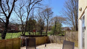 A patio area with a table and chairs, surrounded by wooden fences and trees. - 4 Riverside Cottages (Bridport)