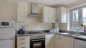 A kitchen with white cabinets, a microwave, a stove, a toaster, and a washing machine. - 4 Riverside Cottages (Bridport)