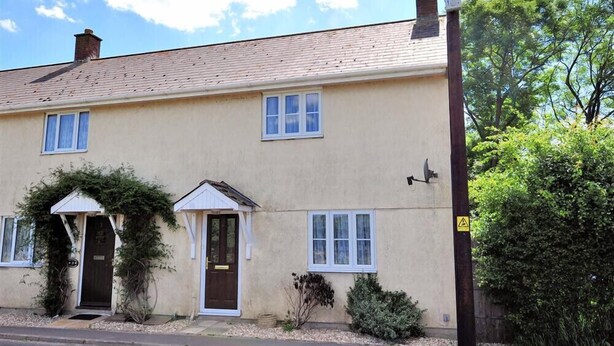 A two-story house with a front porch, a chimney, and a satellite dish. - 4 Riverside Cottages (Bridport)