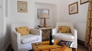 Un salon avec deux fauteuils blancs, une table basse en bois sur laquelle se trouvent une bouteille et des verres, et une lampe.