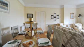 Un coin repas avec une table en bois dressée pour quatre personnes, un lustre et des tableaux encadrés accrochés aux murs.