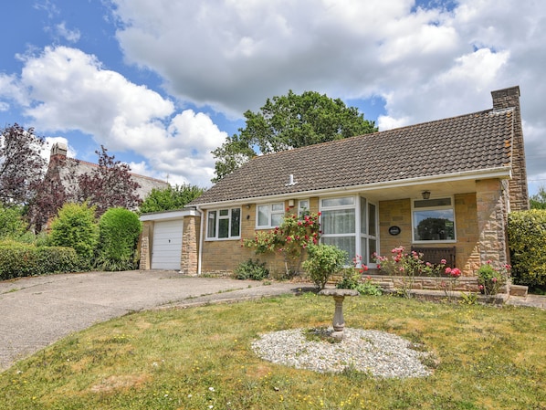 A two-story house with a stone facade, a tiled roof, and a front garden with a birdbath. - Byeways (Axminster)