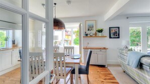 A bright kitchen with white cabinets, a dining table with chairs, and a view of the outside through large windows. - Highpoint Lodge (Lyme Regis)