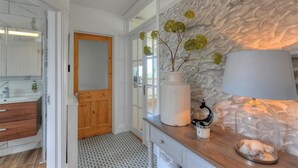 A bathroom with a white vanity, a wooden door, a stone wall, and a lamp on the counter. - Highpoint Lodge (Lyme Regis)