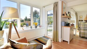 A bright living room with a large window, a wicker chair, a radiator, and a small kitchen area. - Highpoint Lodge (Lyme Regis)
